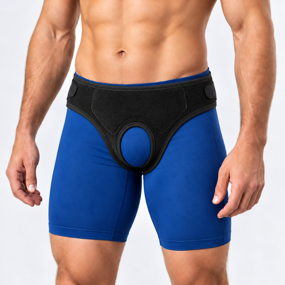 A close-up of a man's lower torso wearing blue athletic briefs with a black Comfort-Truss hernia belt over the front, photographed against a light gray studio background.